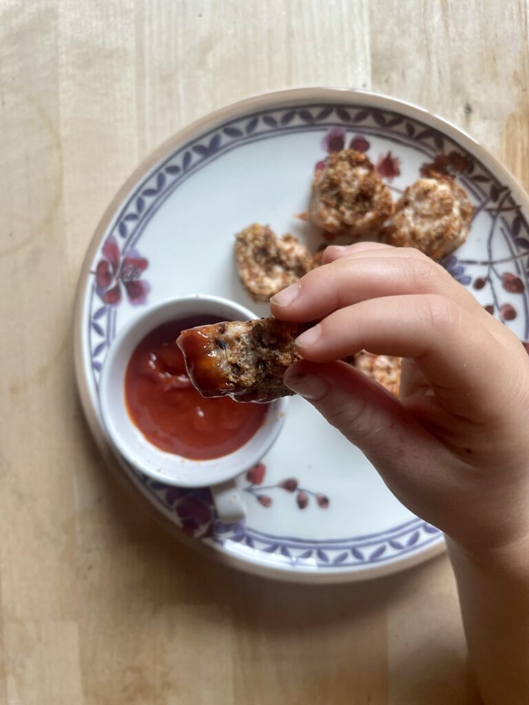 image of child's hand holding a homemade chicken nugget dipped in ketchup