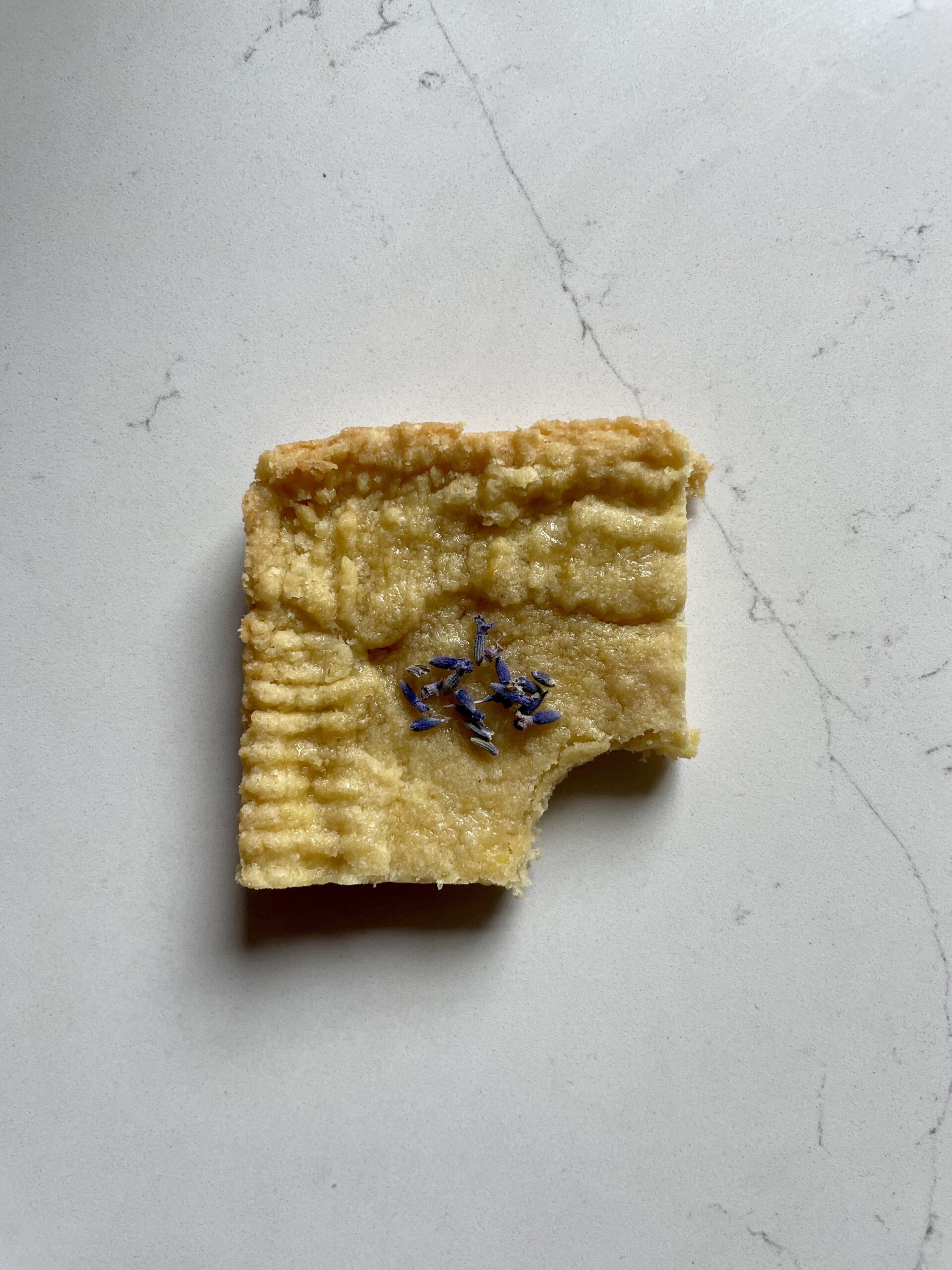 photo of a piece of shortbread with a bite taken out of it, topped with lavender buds