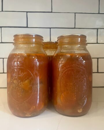 homemade beef stew canned in mason jars in front of subway tile kitchen backsplash