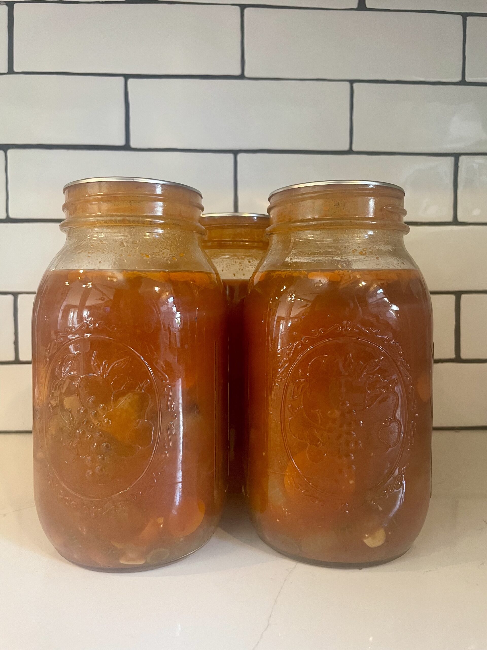 homemade beef stew canned in mason jars in front of subway tile kitchen backsplash