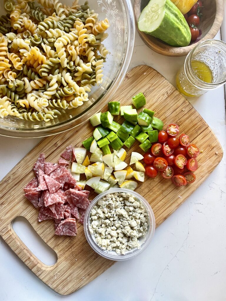 pasta salad ingredients, cucumbers, tomatoes, cheese, salami, dressing